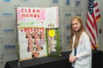 Student poses infront of Clean Hands exhibit.